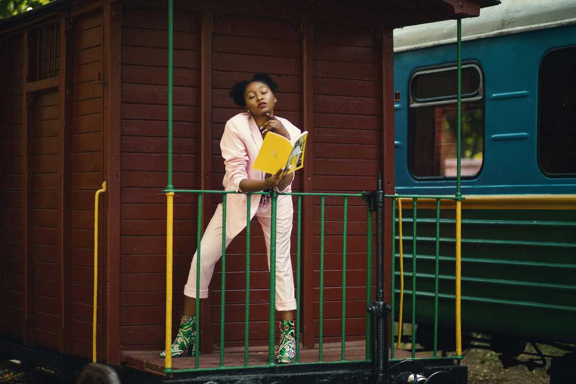 A young woman wearing pink blazer pants and green-heeled shoes holding a yellow-covered book A young woman wearing pink blazer pants and green-heeled shoes holding a yellow-covered book