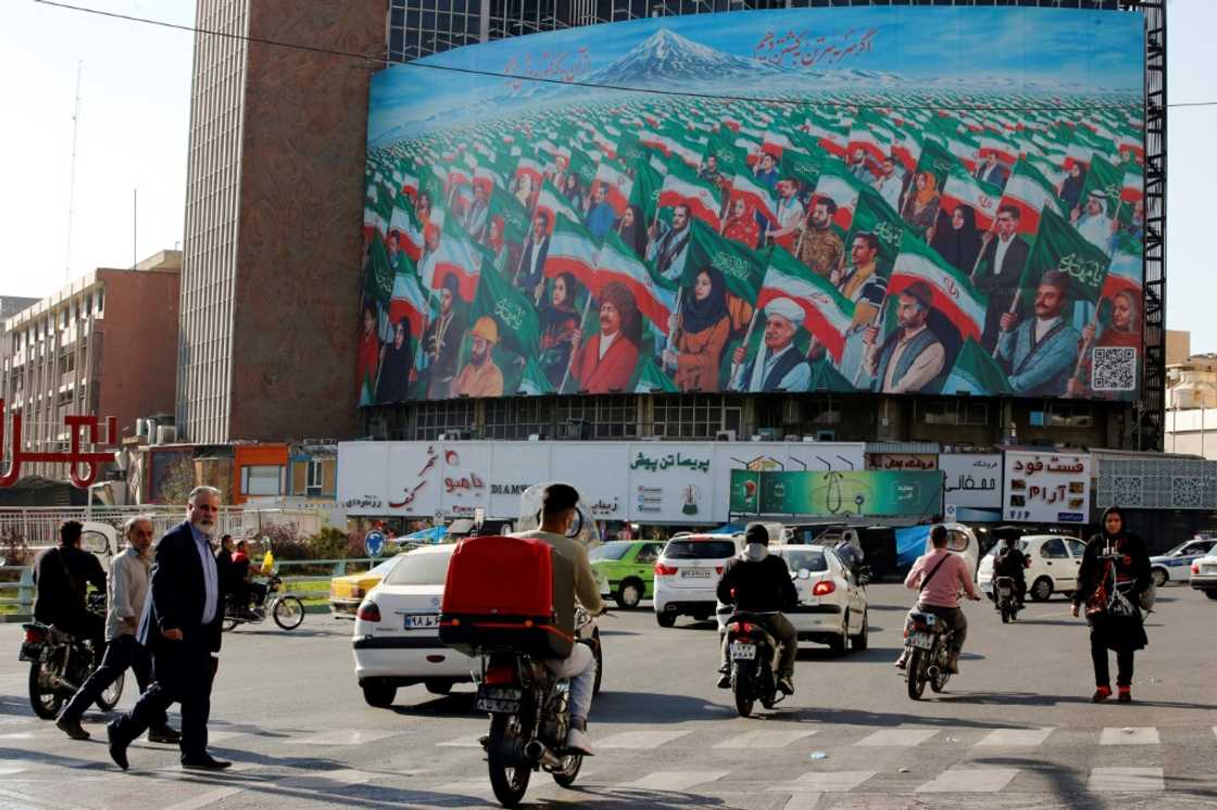 Pedestrians in Tehran's Valiasr Square near a huge billboard depicting Iranians marching with national flags