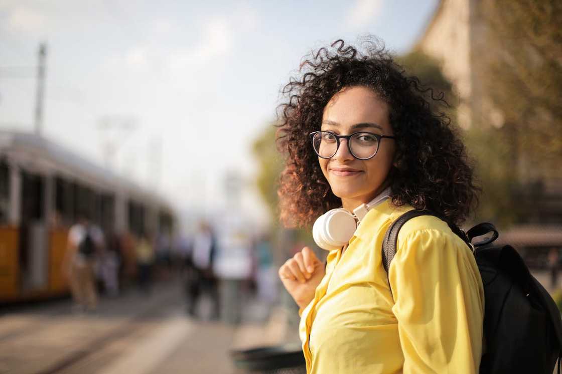 A woman with eyeglasses smiles outside.