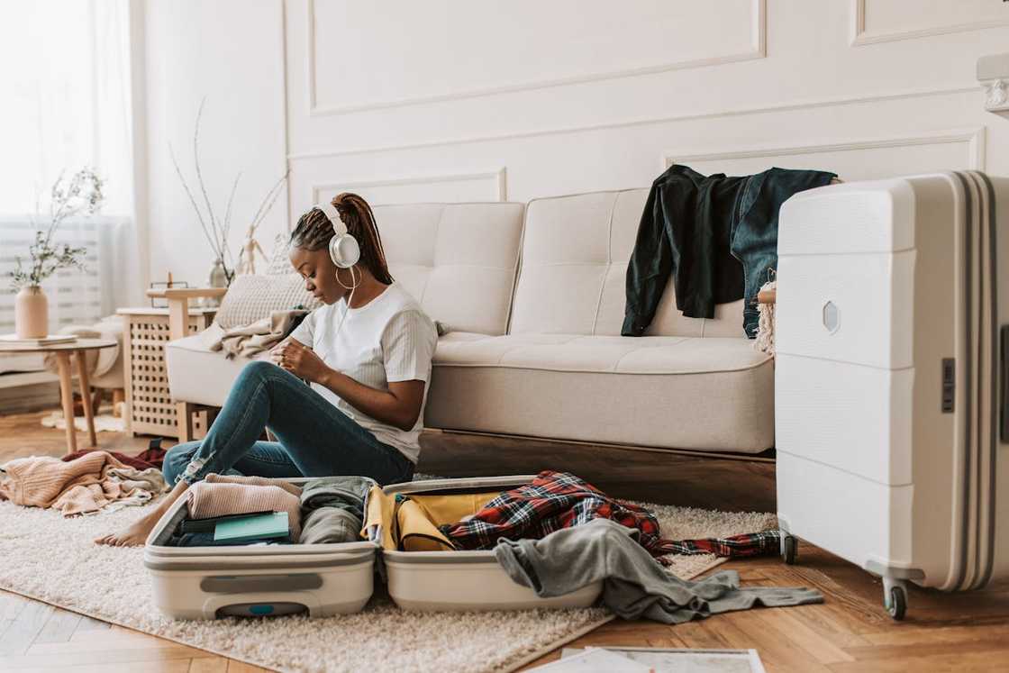 A woman sits on the floor with a messy open suitcase.