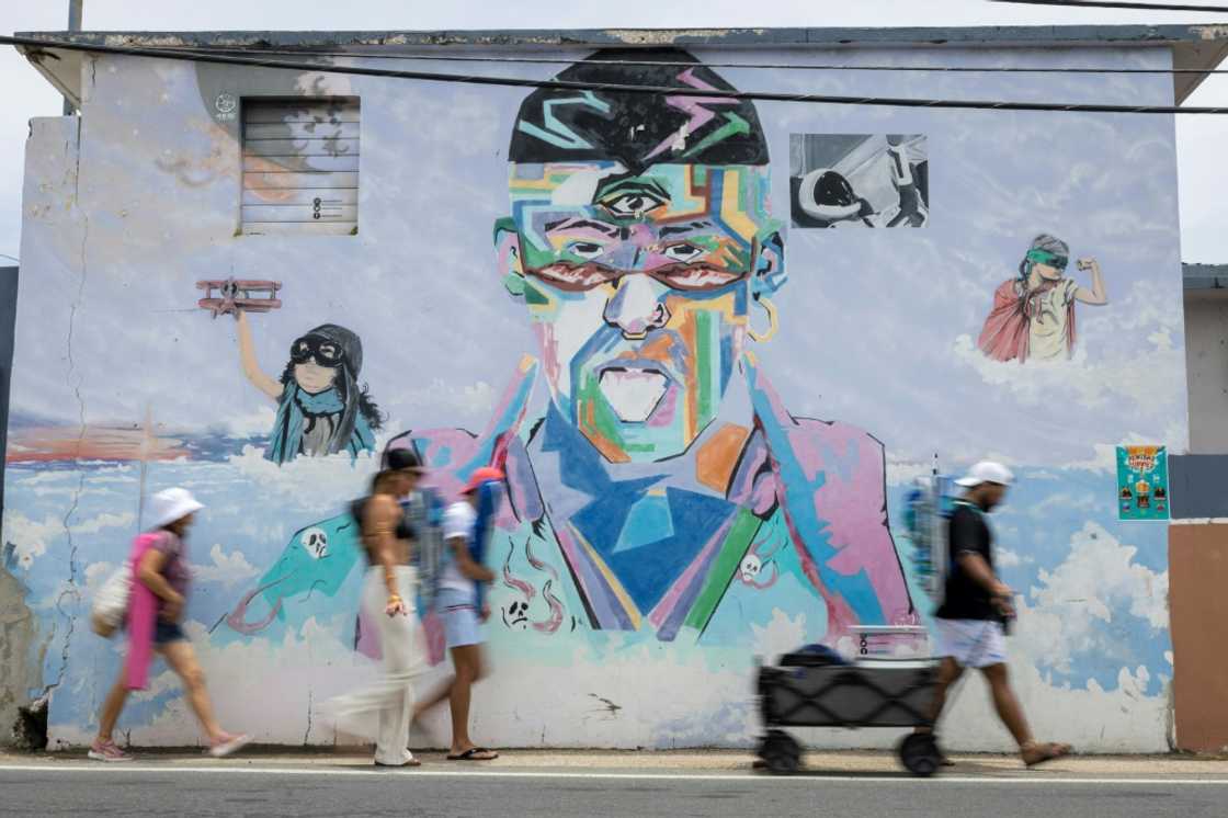 People on their way to the beach walk past a mural of Puerto Rican singer Bad Bunny in Vega Baja, Puerto Rico, the municipality where the global superstar grew up People on their way to the beach walk past a mural of Puerto Rican singer Bad Bunny in Vega Baja, Puerto Rico, the municipality where the global superstar grew up