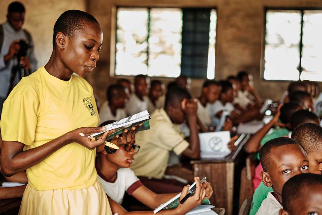 A student in yellow uniform reads a book while standing in class