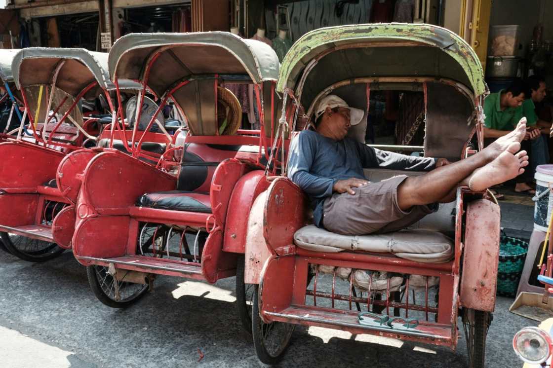 The driver of an Indonesian bechak, a traditional pedicap, sleeps in front of a market in Surakarta, Central Java. The economy of the country cooled slightly in the second quarter of 2024, according to latest data