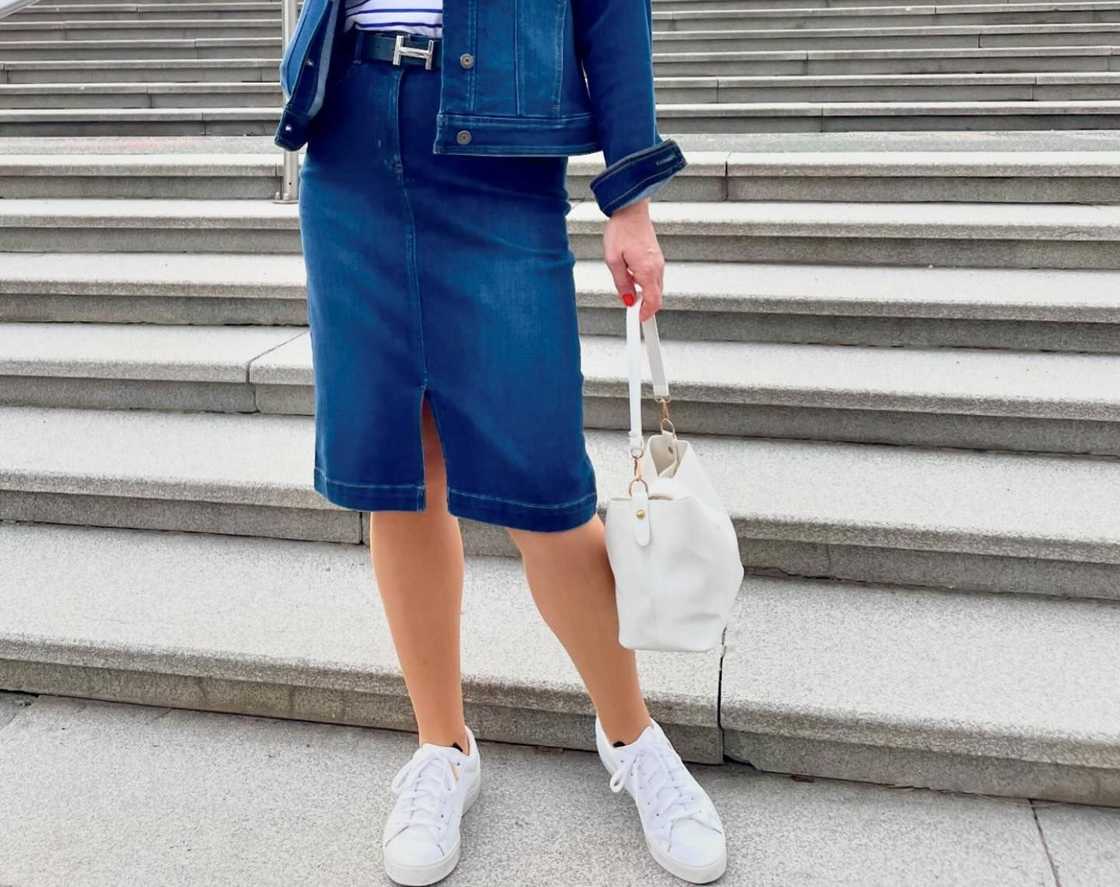 A woman wearing a denim skirt clutches a white handbag