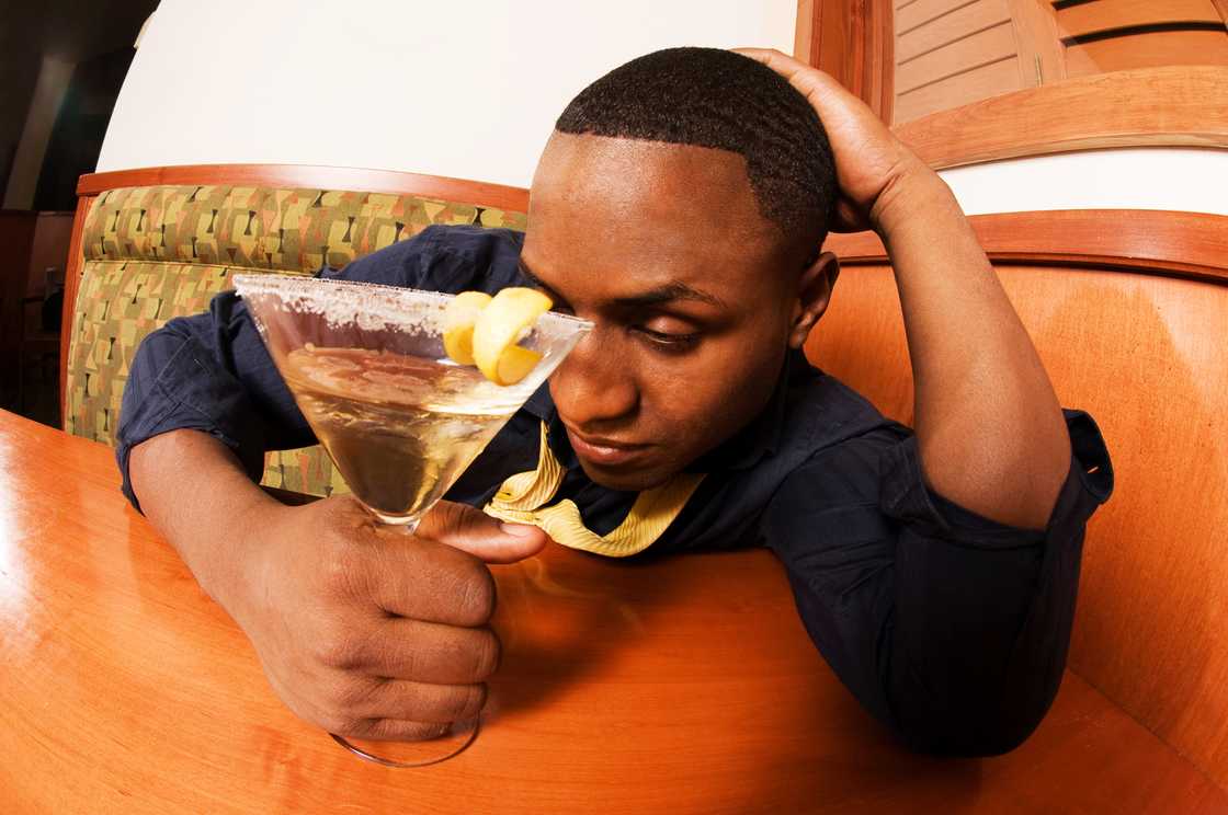 A drunk businessman clutches a martini glass in a bar