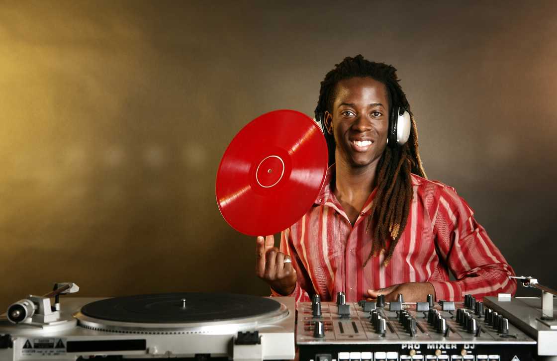 A person wearing headphones and a red striped shirt stands behind DJ equipment.