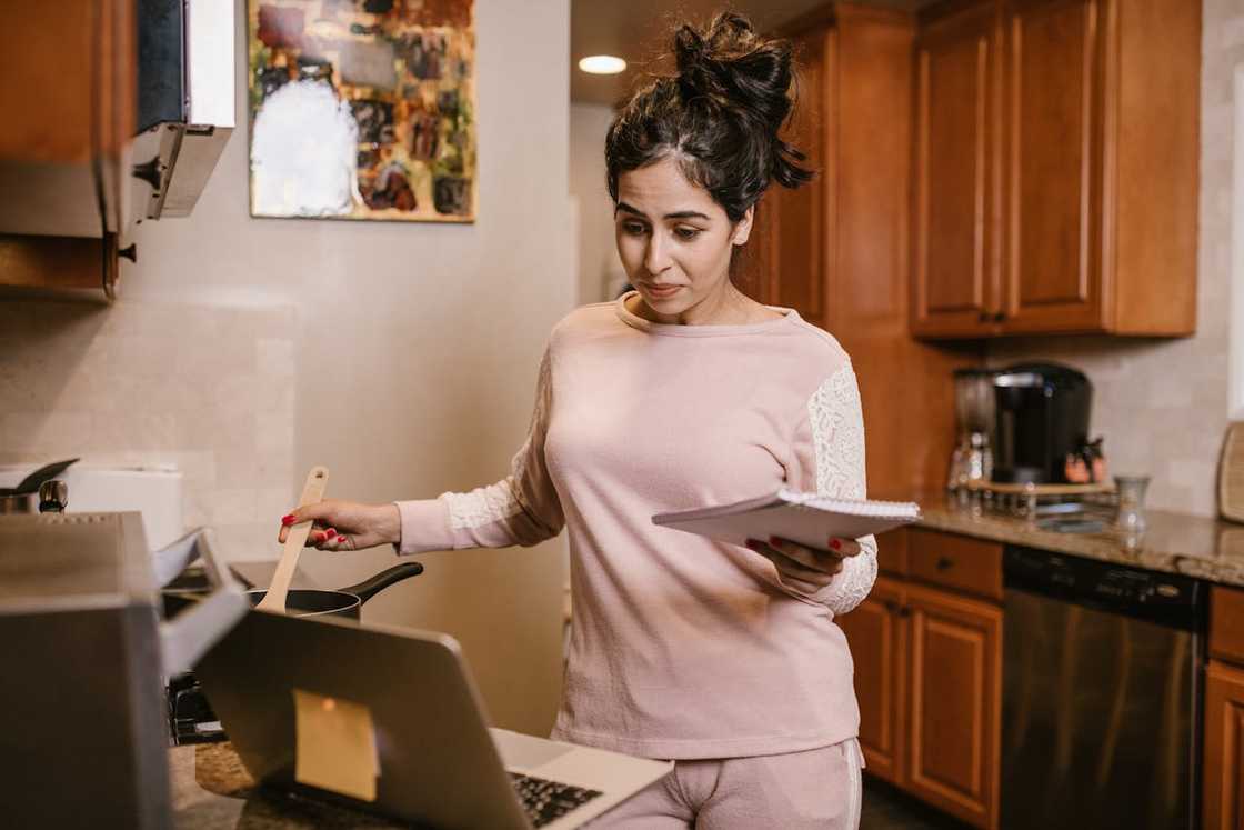 A woman cooking while looking at her laptop.