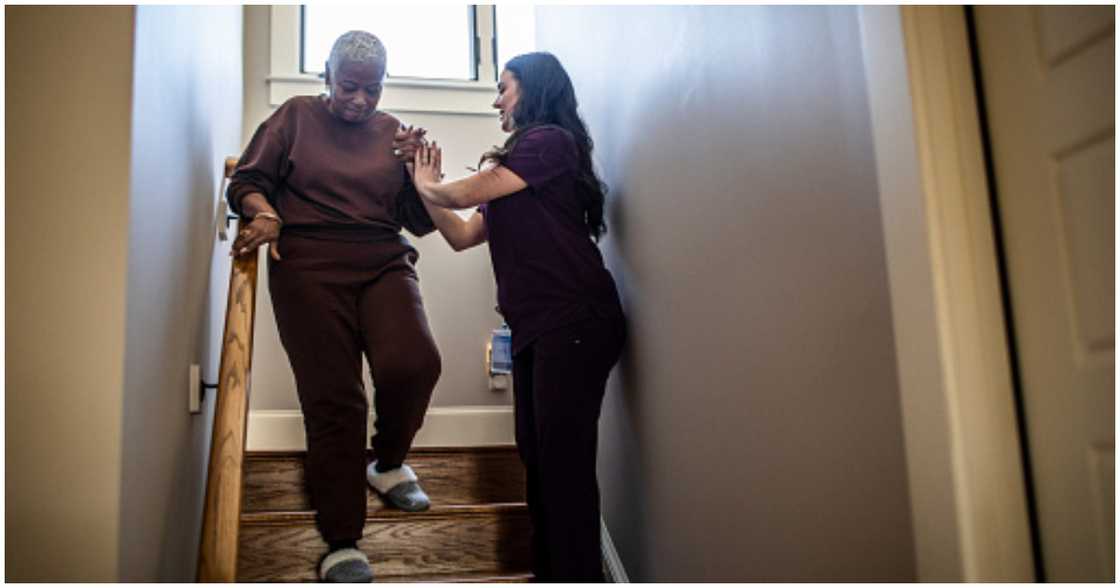 A woman helps an older person down the stairs