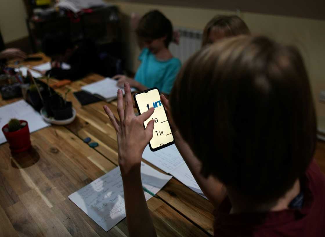 Velimir studies letters on a phone as he sits with other young Russian expats learning Serbian