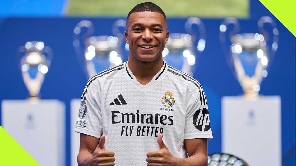Kylian Mbappe strikes for a pose during his presentation as a Real Madrid player with the club's host of trophies in the background. Kylian Mbappe strikes for a pose during his presentation as a Real Madrid player with the club's host of trophies in the background.