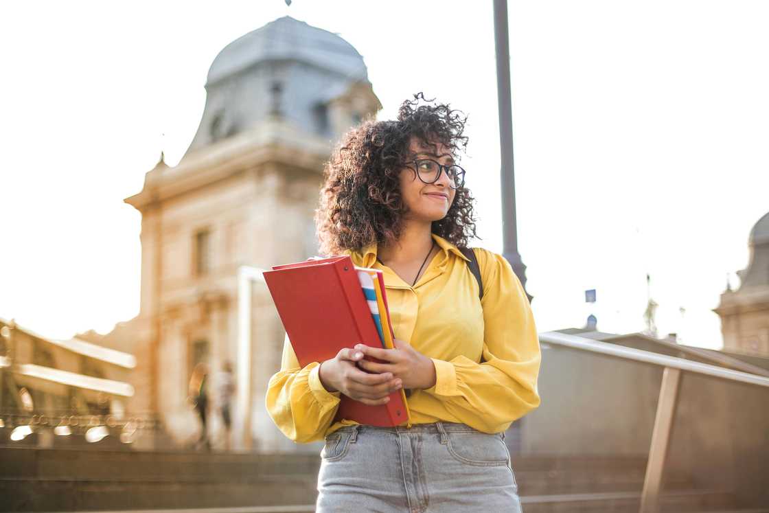 A female college student in a yellow shirt is pictured holding books