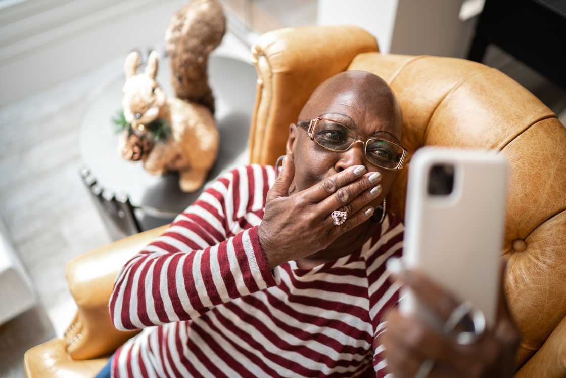 A shocked woman holding a phone indoors.