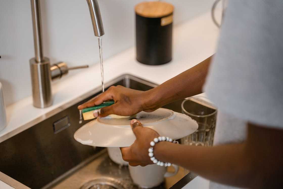 Hands washing a plate under running water in a kitchen sink. Hands washing a plate under running water in a kitchen sink.