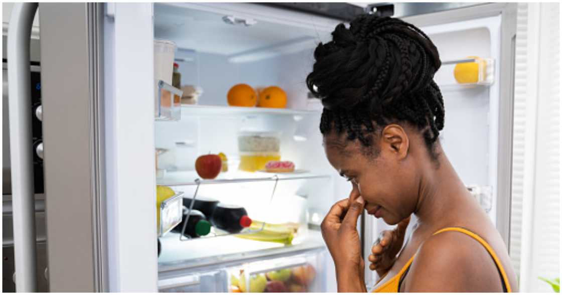 A lady holds her nose because of a bad smell from her fridge A lady holds her nose because of a bad smell from her fridge