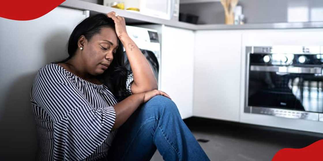 Photo of depressed mature woman sitting on the ground at home