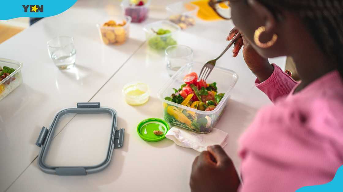 A young woman eats salads out of a plastic container. A young woman eats salads out of a plastic container.