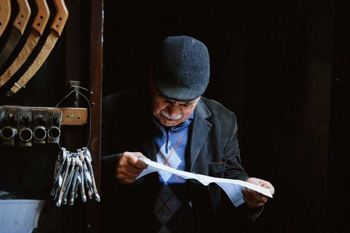An elderly man reads a document inside a small workshop. An elderly man reads a document inside a small workshop.