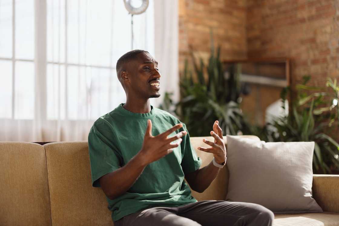 Young adult man gesturing while speaking from his couch in a bright living room