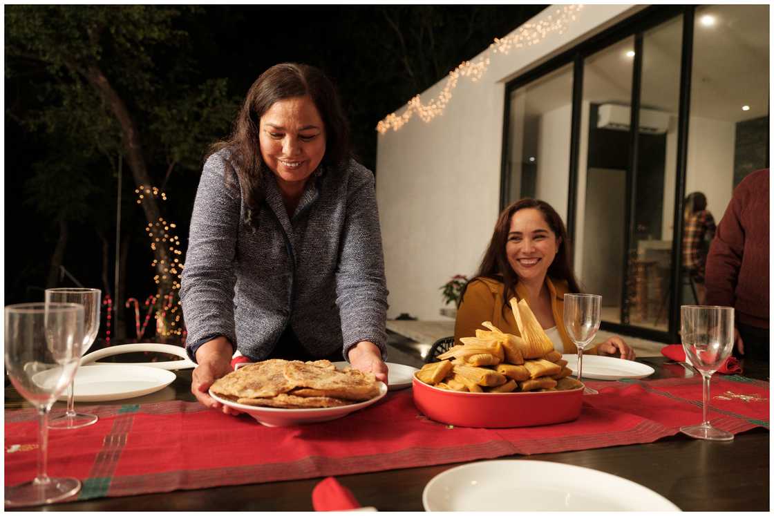 A lady is smiling and putting Christmas food on a table.