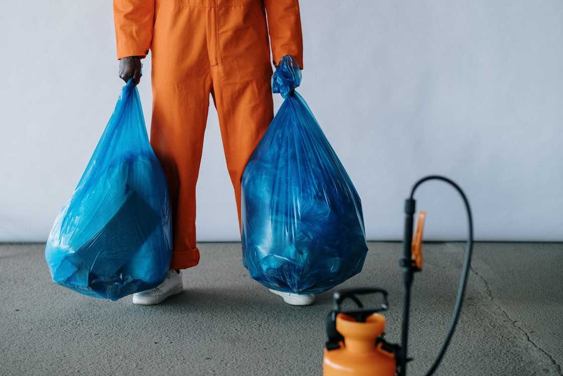 A person in protective clothing carries two large blue trash bags. A person in protective clothing carries two large blue trash bags.