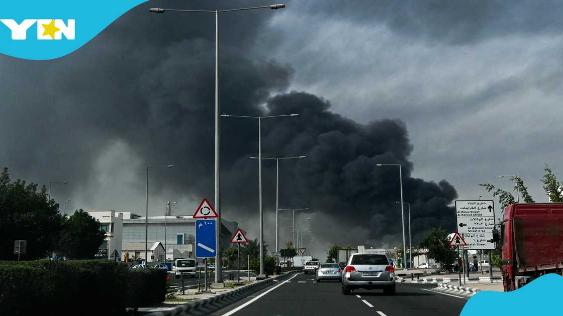 Motorists drive past a plume of smoke rising from a reported Iranian strike in the industrial district of Doha on March 1, 2026