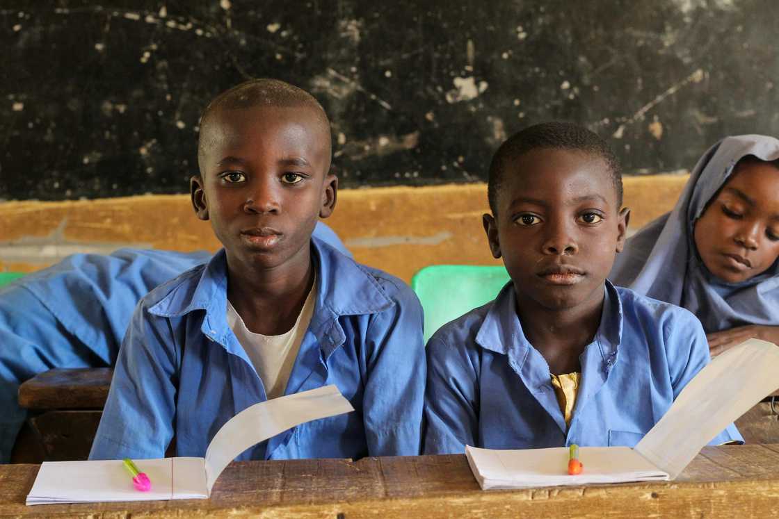 Little children in blue uniforms are sitting at their desks inside a classroom