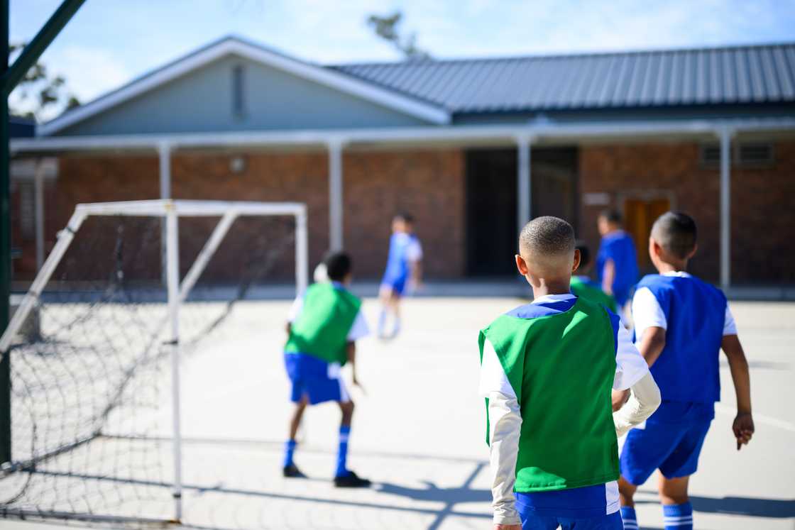 Children play soccer on a school court, with one defending the goal.