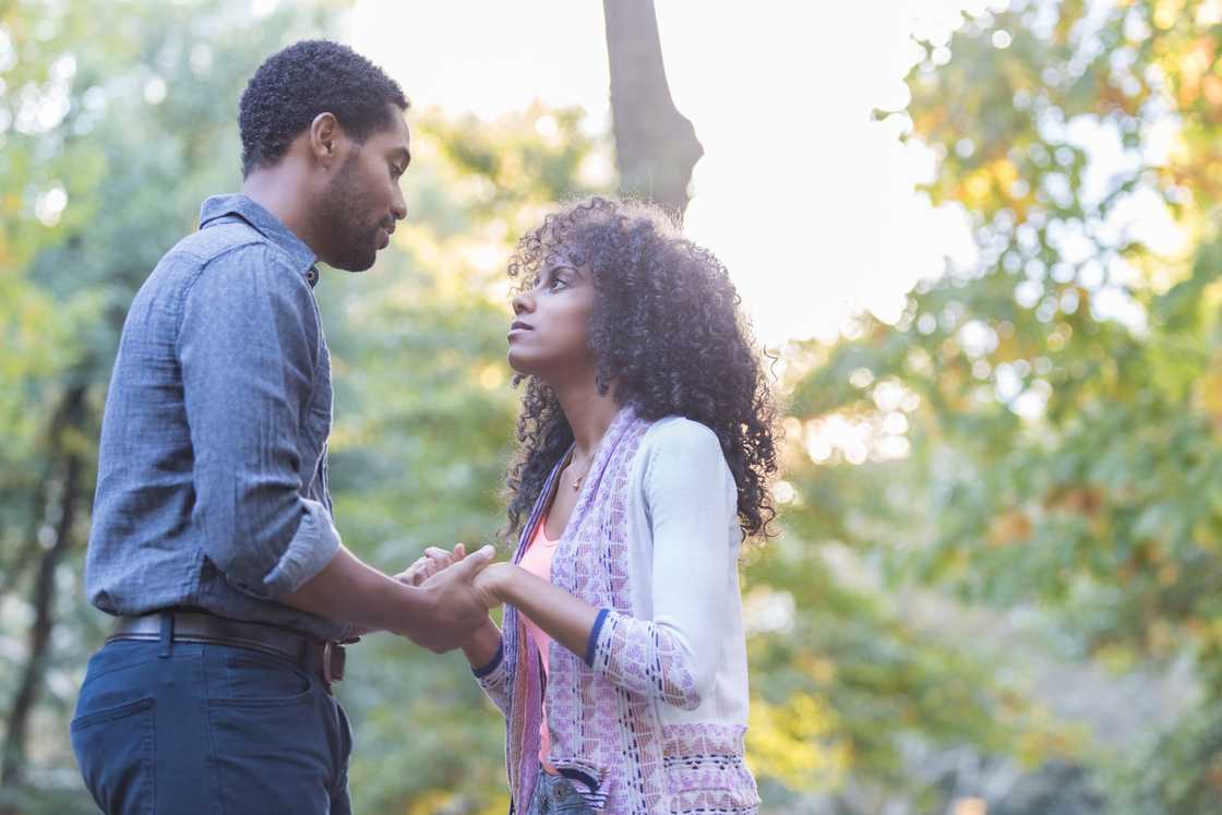 A young couple stands outside in the sunlight holding hands