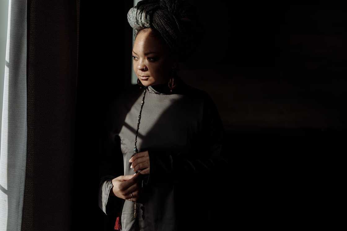 A woman standing by a window in low light, looking thoughtful. A woman standing by a window in low light, looking thoughtful.