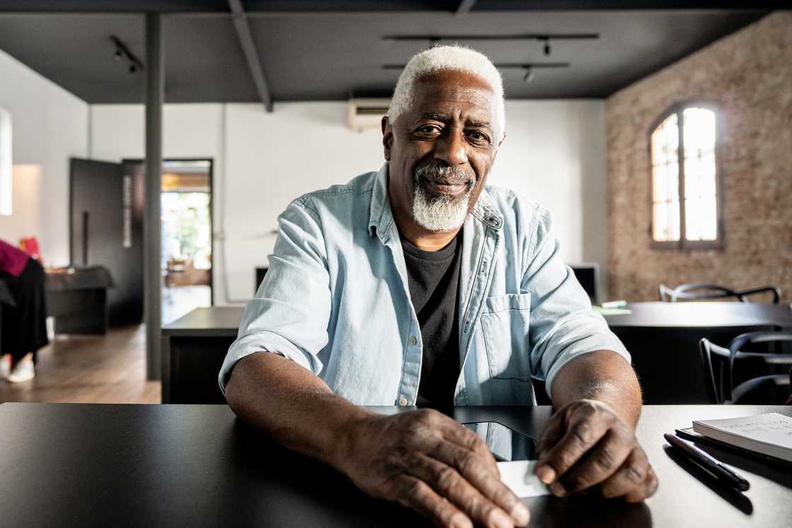 Older person with grey hair and beard smiles while seated.