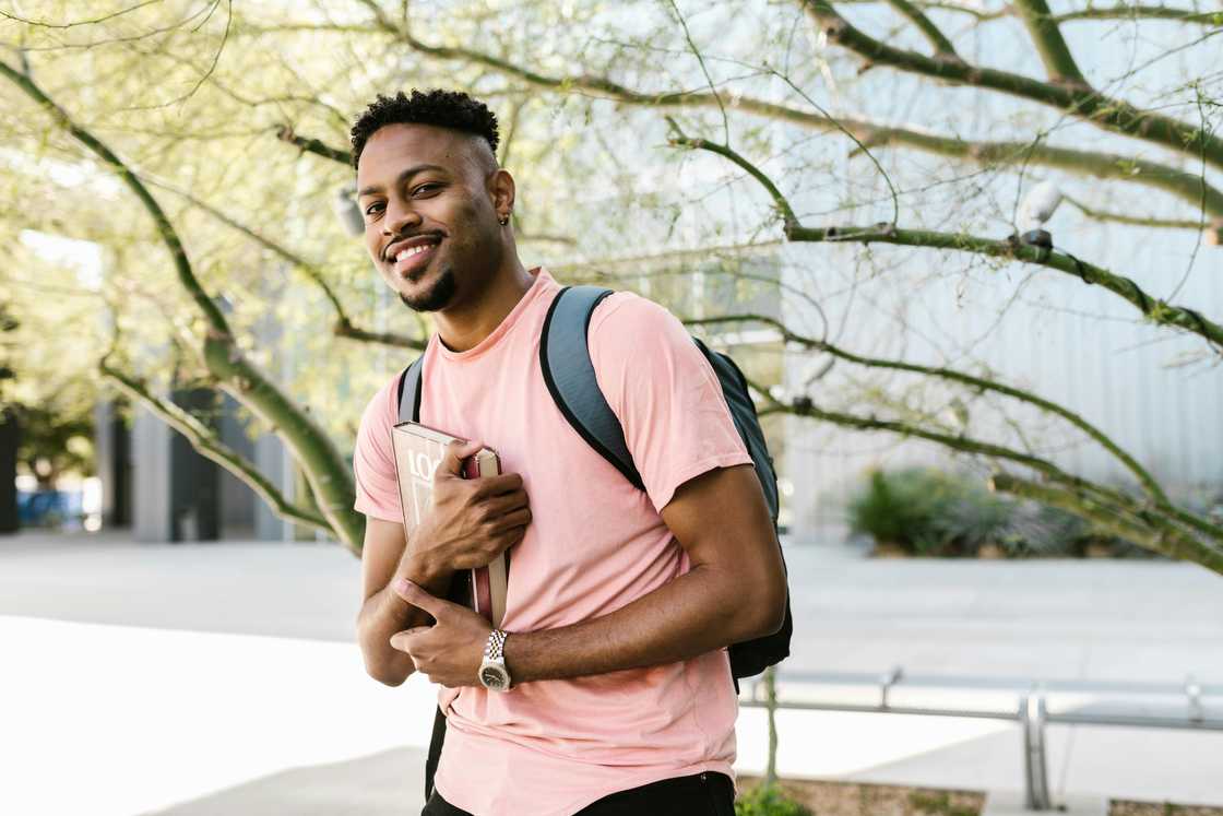 A male college student smiling while holding a book