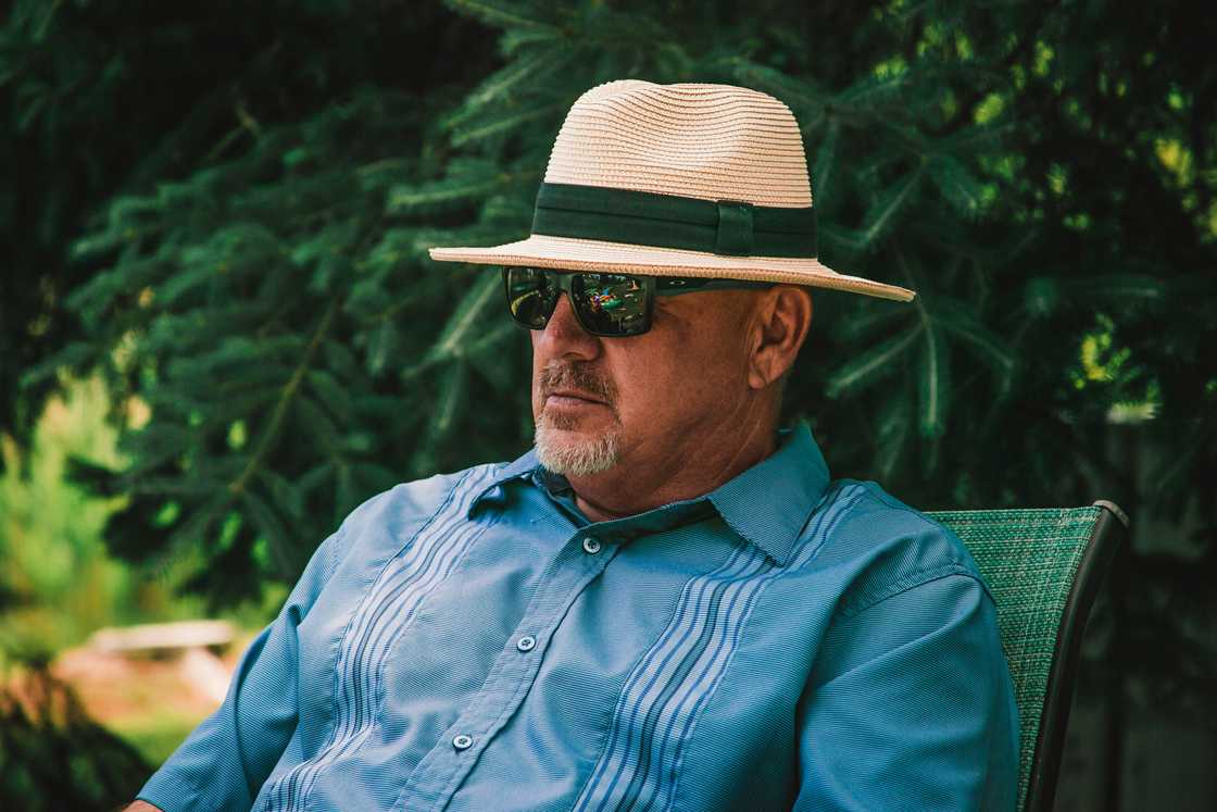 A man is dressed in a blue shirt, sunglasses, and a Panama hat A man is dressed in a blue shirt, sunglasses, and a Panama hat