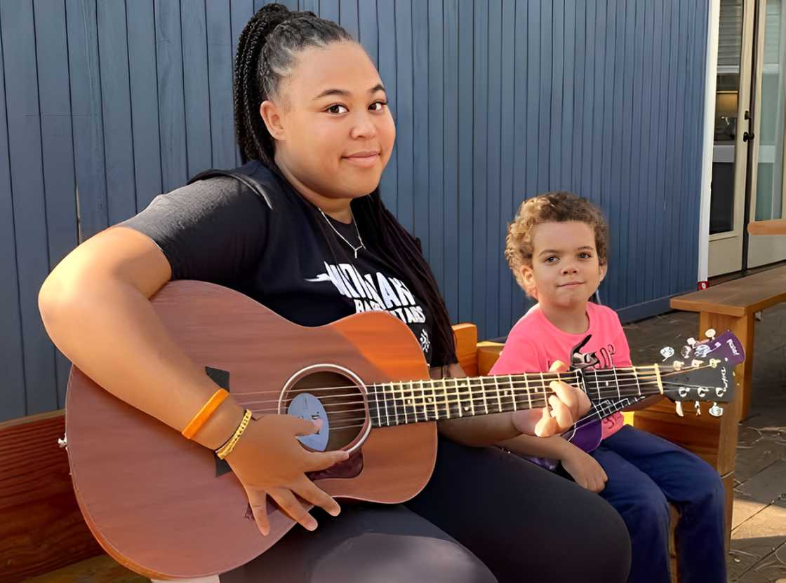 Amara Trinity Lawrence playing a guitar next to a kid Amara Trinity Lawrence playing a guitar next to a kid