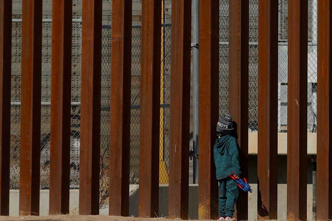 A Venezuelan child migrant stands by the wall along the Mexican-US border