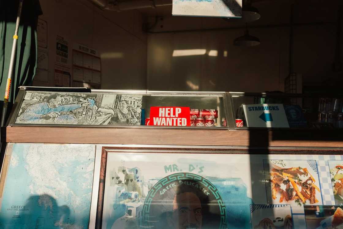 A small food stall counter with a red "Help Wanted" sign displayed behind glass.