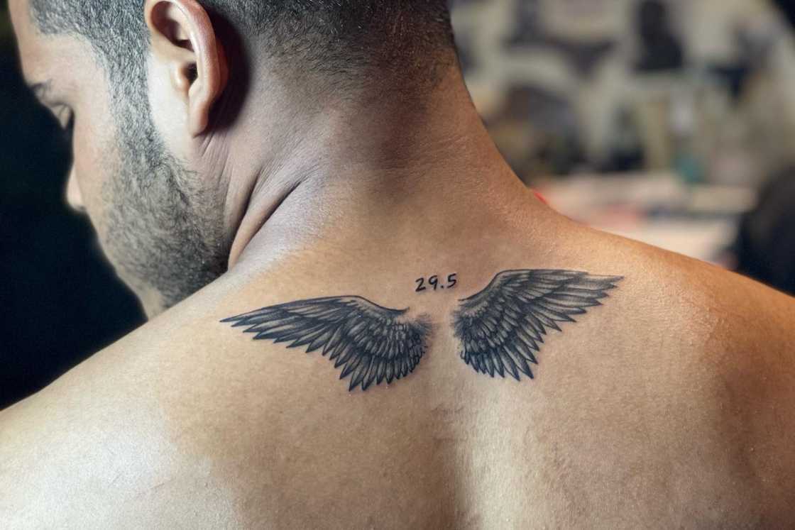 A man is donning a small wing tattoo on his upper back A man is donning a small wing tattoo on his upper back