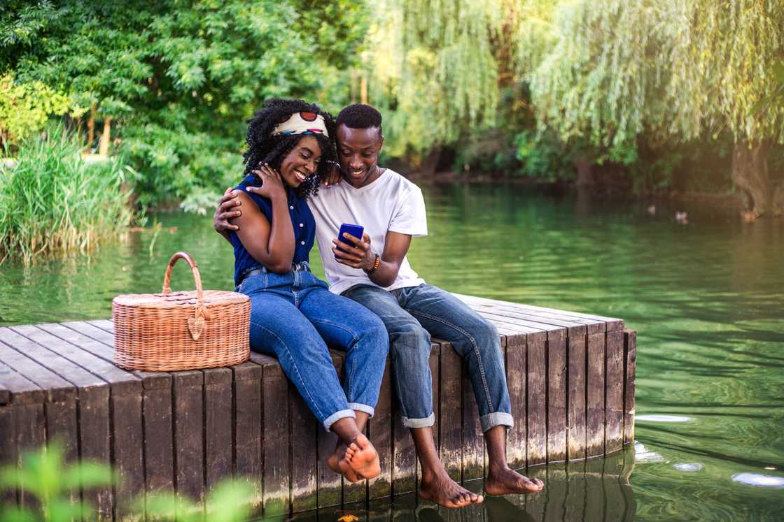 A young black couple sitting on the lake's pier with a picnic basket A young black couple sitting on the lake's pier with a picnic basket