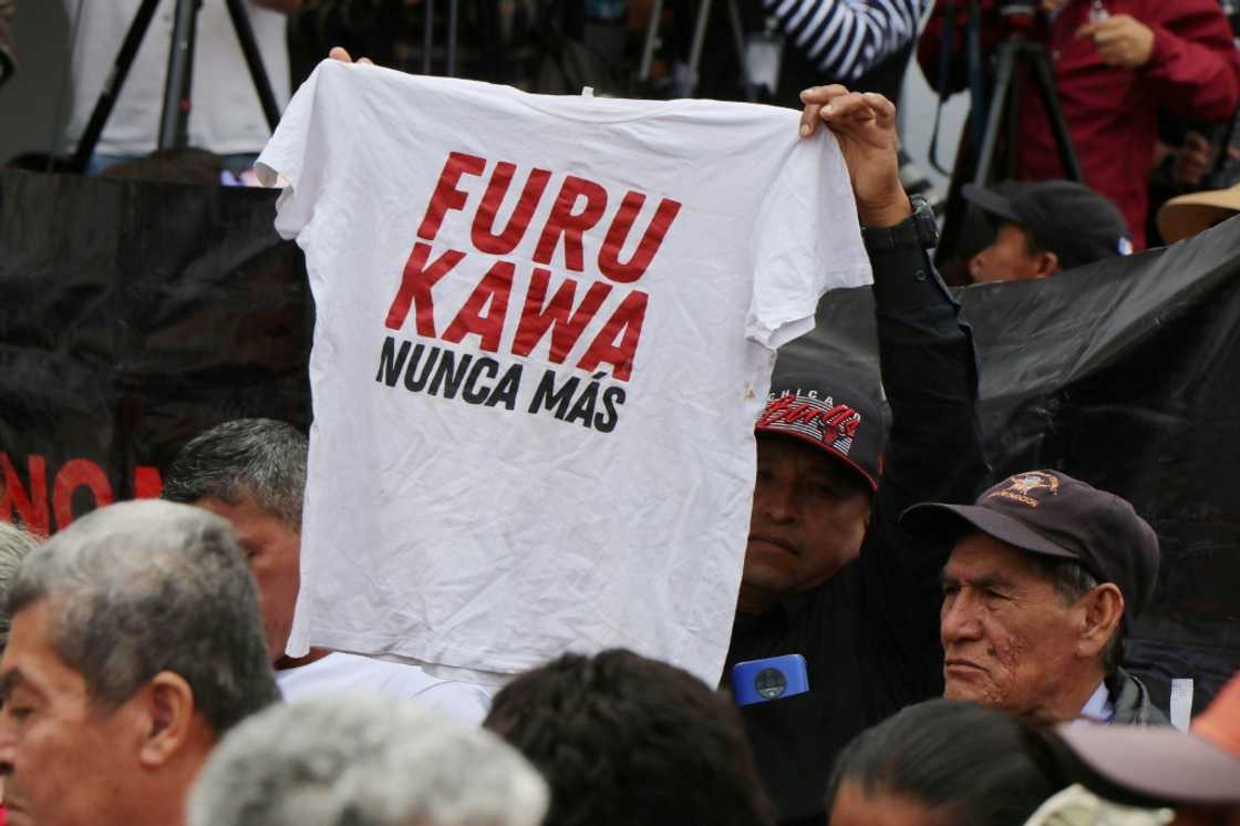 A man in Ecuador holds up a shirt with the slogan 'Furukawa, never again,' alluding to a Japanese textile firm found to have abused its workers