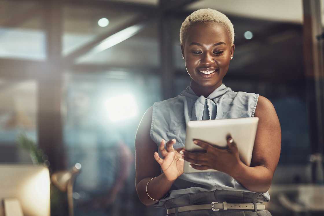 A Black woman smiles while holding a tablet