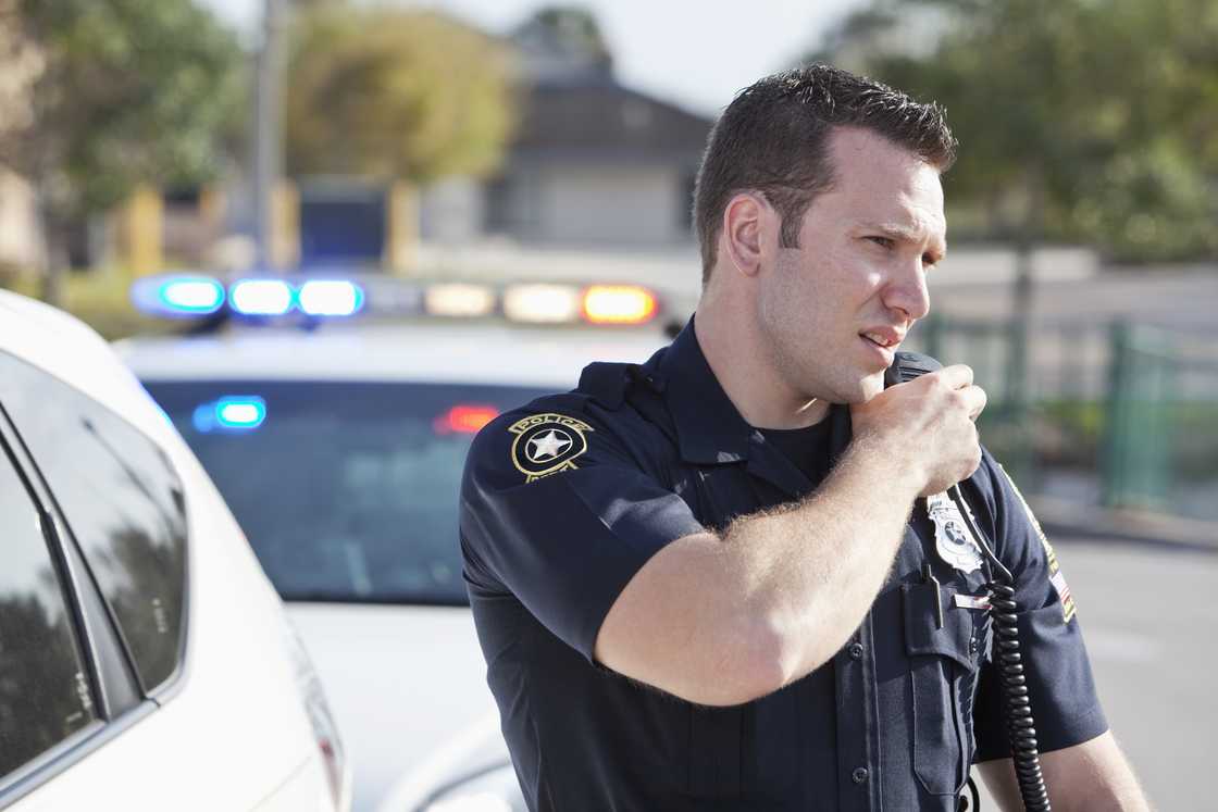 A male police officer standing outdoors, reaching for a radio. A male police officer standing outdoors, reaching for a radio.