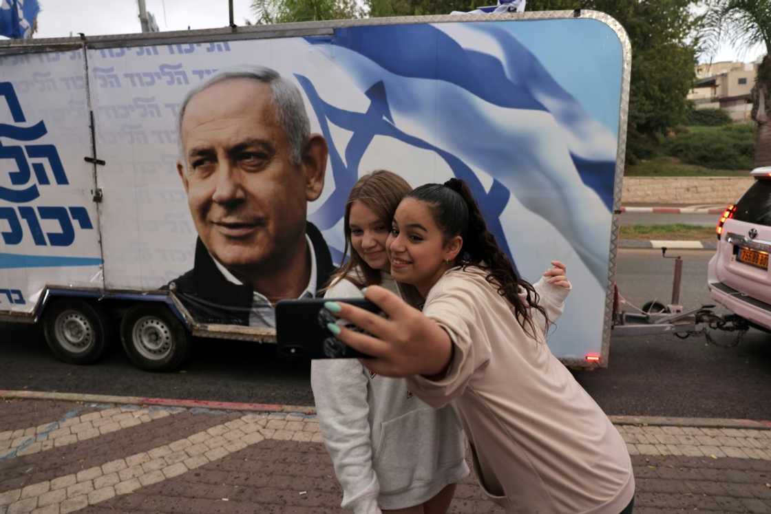 Two girls pose for a selfie photo before a vehicle showing Israel's former prime minister Benjamin Netanyahu, ahead of November 1 general elections Two girls pose for a selfie photo before a vehicle showing Israel's former prime minister Benjamin Netanyahu, ahead of November 1 general elections