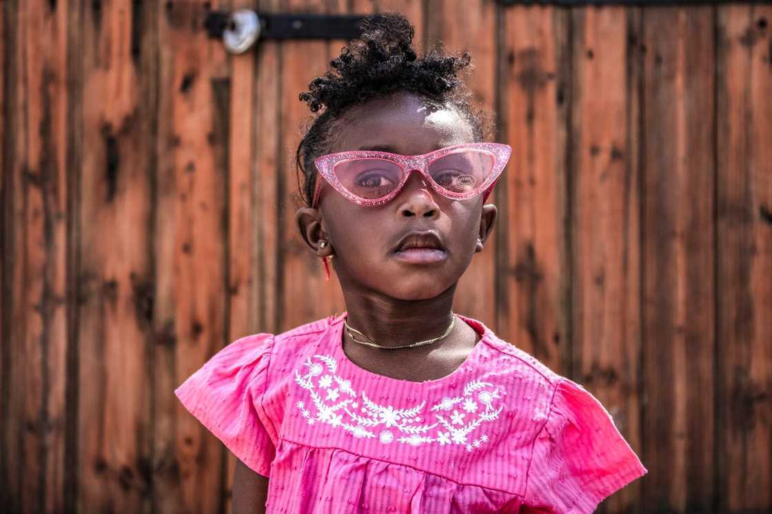 A young girl wears pink glasses and looks ahead confidently. A young girl wears pink glasses and looks ahead confidently.
