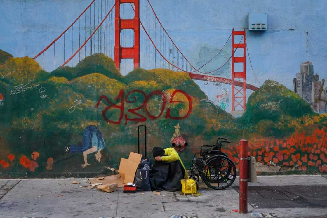 A homeless person leans against a mural of the Golden Gate Bridge near APEC Summit headquarters in San Francisco, California on November 11, 2023 A homeless person leans against a mural of the Golden Gate Bridge near APEC Summit headquarters in San Francisco, California on November 11, 2023