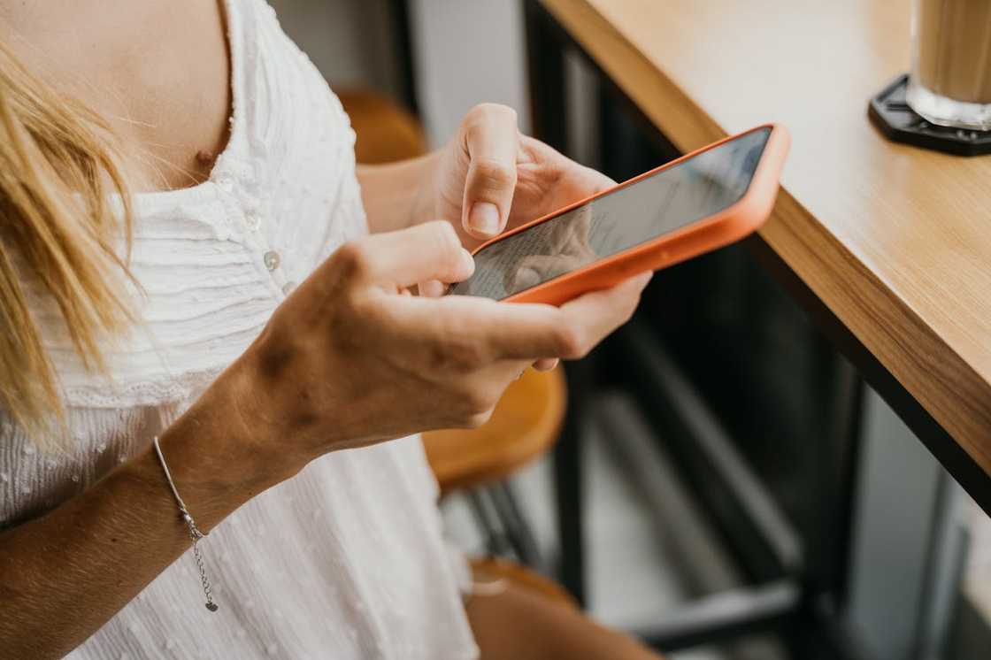 Close-up of a person holding and using a smartphone at a table.