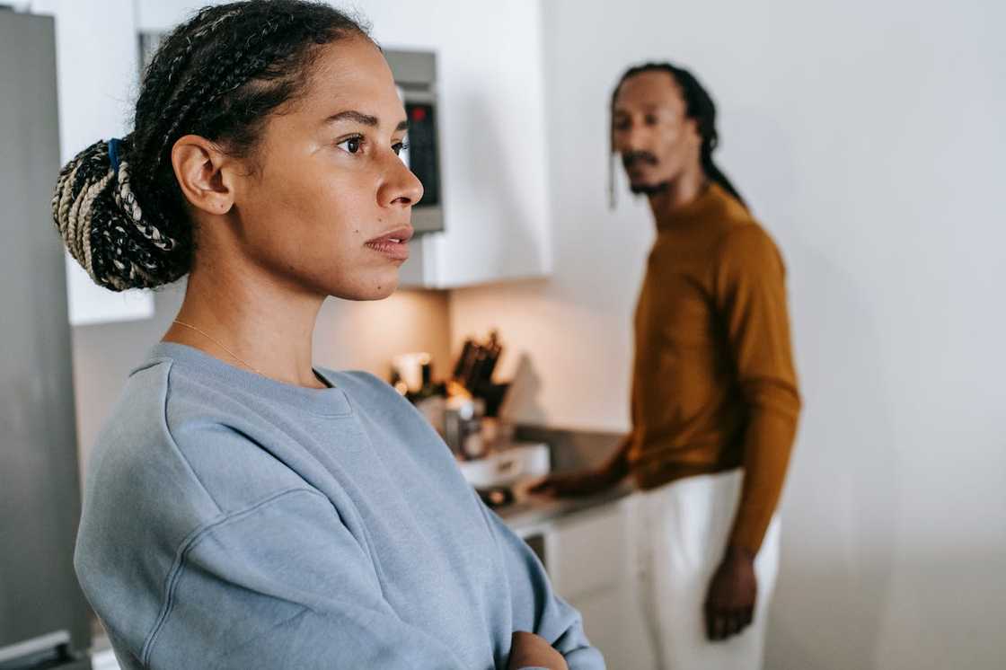 Woman looking tense as a man stands behind her in a kitchen.