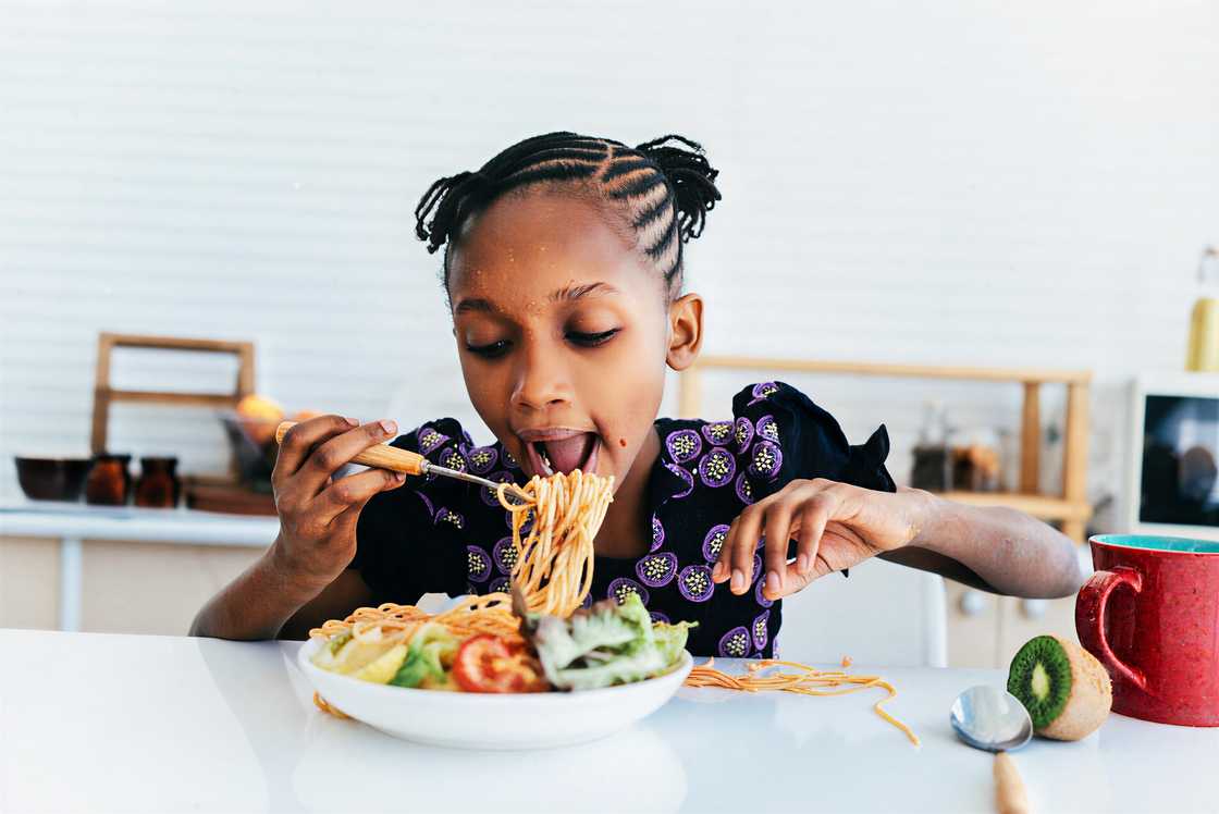 An African girl enjoys eating spaghetti