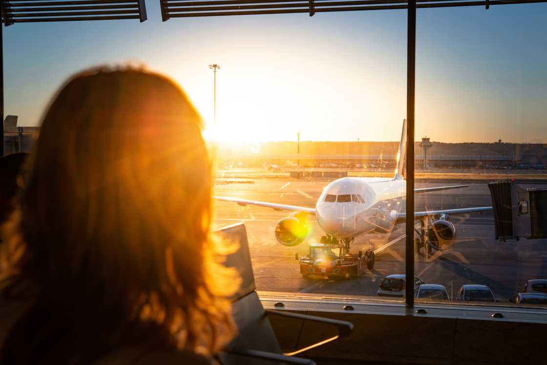Airport terminal sunrise; calm traveller gazes out window at parked aircraft. Airport terminal sunrise; calm traveller gazes out window at parked aircraft.