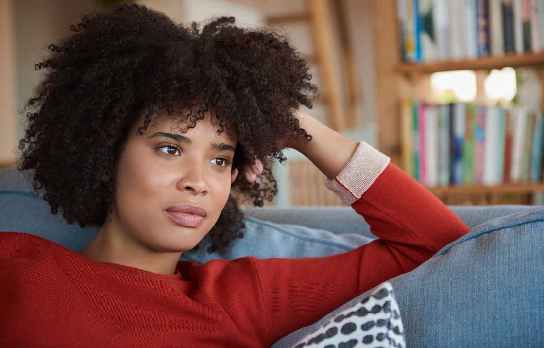 A young woman lost in thought and smiling while sitting on a sofa