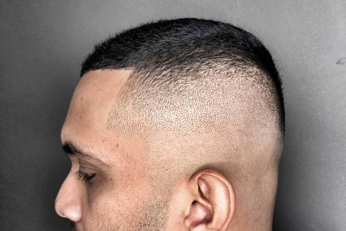 A man with an undercut is leaning against a grey background