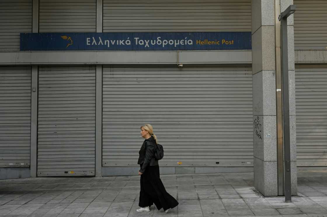 A woman walks past a closed post office during a 24-hour strike in Athens